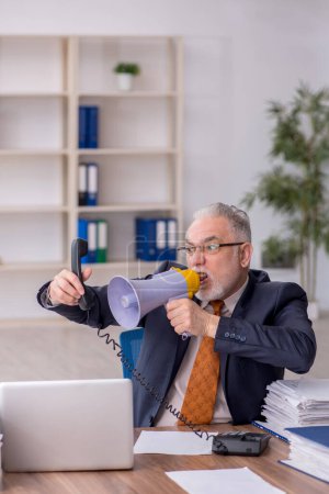 Photo for Old employee holding megaphone at workplace - Royalty Free Image