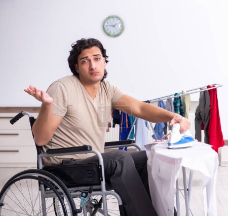 Foto de El joven en silla de ruedas haciendo planchado en casa - Imagen libre de derechos
