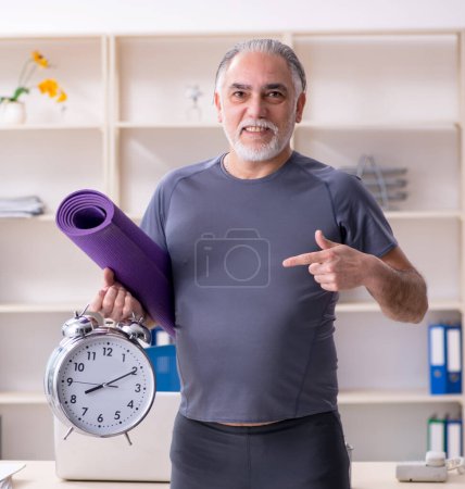 Téléchargez les photos : The white bearded old man employee doing exercises in the office - en image libre de droit