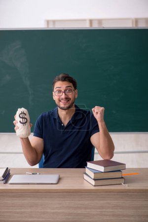 Photo for Young teacher holding moneybag in the classroom - Royalty Free Image
