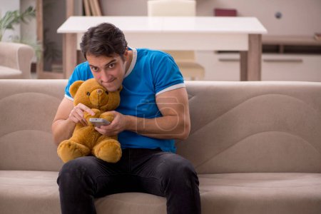 Foto de Joven sentado con oso juguete en casa - Imagen libre de derechos