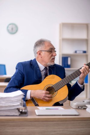 Foto de Old employee playing guitar in the office - Imagen libre de derechos