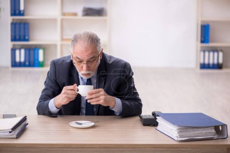 Téléchargez les photos : Old employee drinking tea at workplace - en image libre de droit
