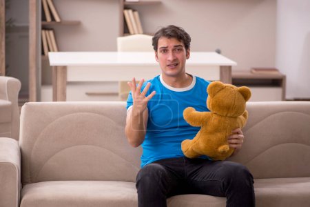 Foto de Joven sentado con oso juguete en casa - Imagen libre de derechos