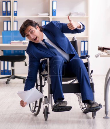 Téléchargez les photos : Le jeune employé masculin en fauteuil roulant travaillant dans le bureau - en image libre de droit