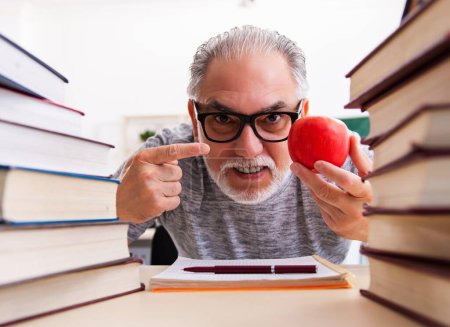 Téléchargez les photos : Étudiant senior mangeant de la pomme pendant la préparation à l'examen - en image libre de droit