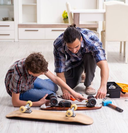 Téléchargez les photos : Le jeune père réparant skateboard avec son fils à la maison - en image libre de droit