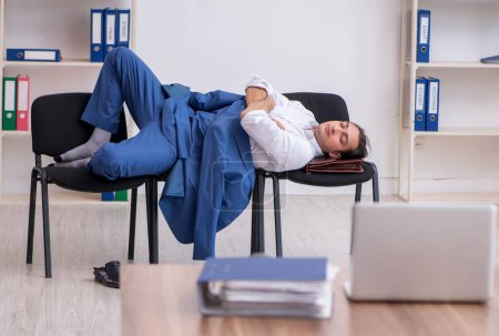 Téléchargez les photos : Jeune employé dormant dans le bureau sur des chaises - en image libre de droit
