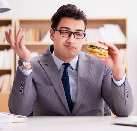 Téléchargez les photos : L'homme d'affaires drôle affamé manger sandwich junk food - en image libre de droit