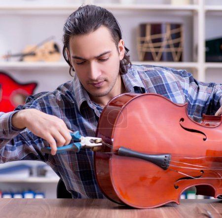 Photo for The young handsome repairman repairing cello - Royalty Free Image