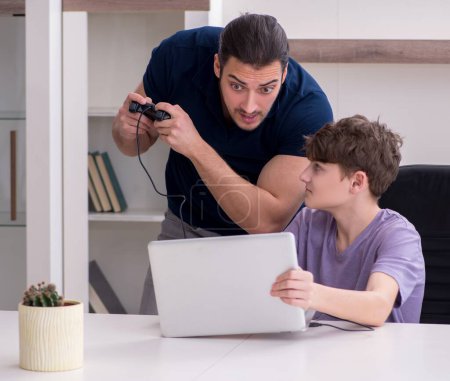 Téléchargez les photos : Père et écolier jouant à des jeux informatiques à la maison - en image libre de droit