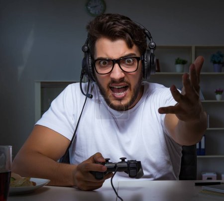 Téléchargez les photos : Le jeune homme jouant à des jeux de longues heures en retard au bureau - en image libre de droit