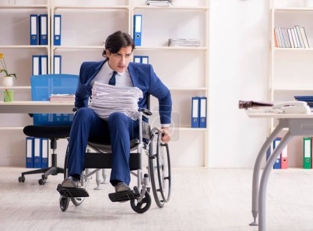 Téléchargez les photos : Le jeune employé masculin en fauteuil roulant travaillant dans le bureau - en image libre de droit