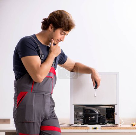 Téléchargez les photos : Le jeune entrepreneur beau réparer réfrigérateur - en image libre de droit