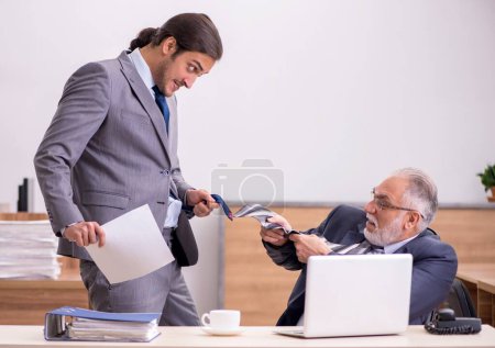 Foto de Viejo jefe masculino y joven asistente masculino en la oficina - Imagen libre de derechos