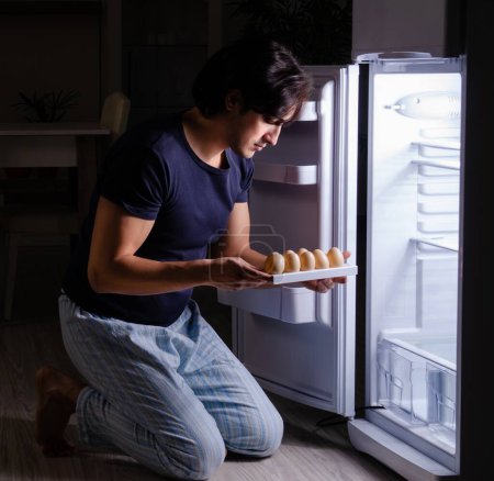 Téléchargez les photos : L'homme rompt son régime la nuit près du frigo - en image libre de droit