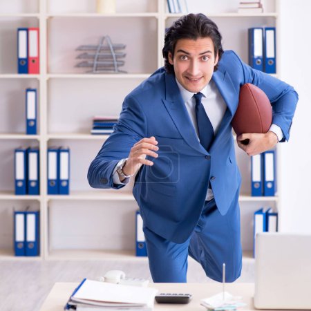 Téléchargez les photos : Le jeune homme d'affaires beau avec ballon de rugby dans le bureau - en image libre de droit