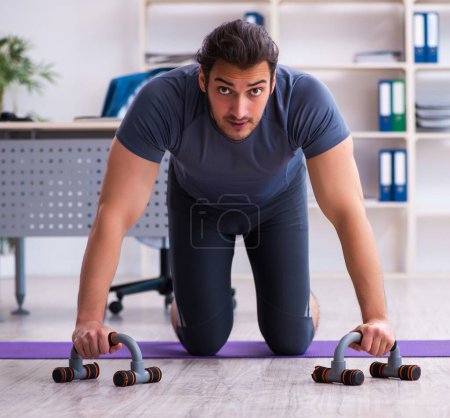 Photo for Young male employee doing sport exercises in the office - Royalty Free Image