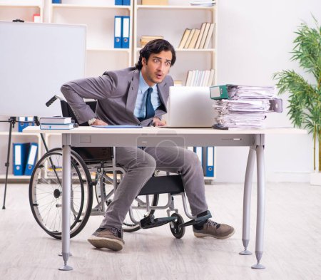 Foto de The young handsome employee in wheelchair at the office - Imagen libre de derechos
