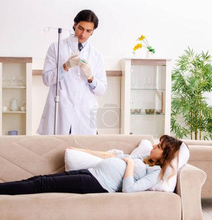 Foto de El joven médico guapo visitando a la mujer embarazada en casa - Imagen libre de derechos