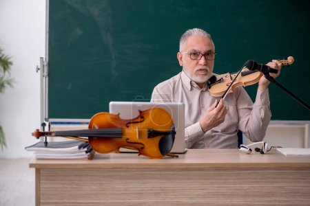 Photo for Old teacher playing violin in the classroom - Royalty Free Image