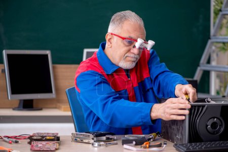 Téléchargez les photos : Vieux réparateur masculin réparant des ordinateurs dans la salle de classe - en image libre de droit