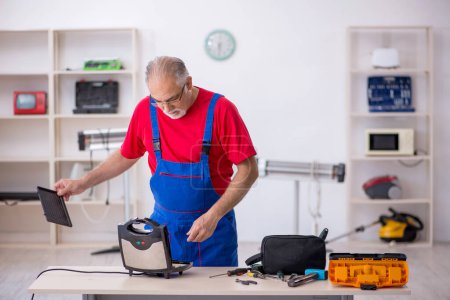 Foto de Viejo reparador masculino reparando sandwichera en taller - Imagen libre de derechos