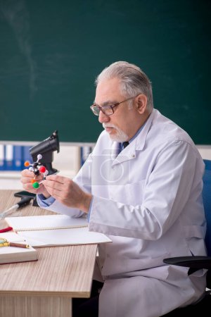 Téléchargez les photos : Old chemist teacher sitting in the classroom - en image libre de droit