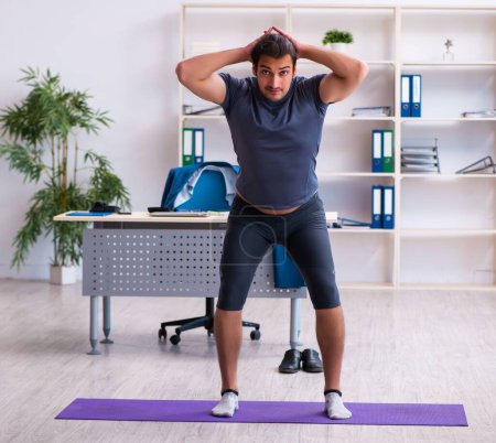 Foto de Joven empleado masculino haciendo ejercicios deportivos en la oficina - Imagen libre de derechos