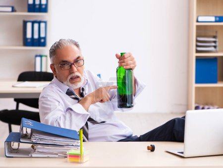 Téléchargez les photos : Vieil homme d'affaires buvant de l'alcool au bureau - en image libre de droit