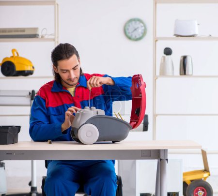 Photo for The young male contractor repairing vacuum cleaner at workshop - Royalty Free Image