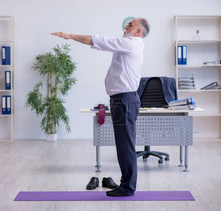 Foto de Empleado anciano haciendo ejercicios físicos durante el descanso - Imagen libre de derechos