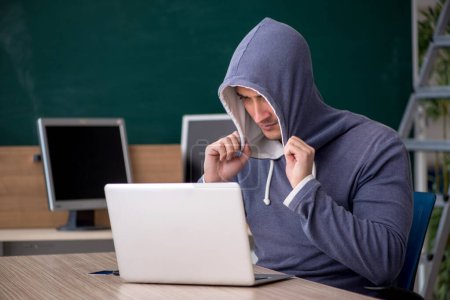 Téléchargez les photos : Jeune hacker assis dans la salle de classe - en image libre de droit