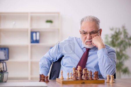 Téléchargez les photos : Vieil employé masculin jouant aux échecs dans le bureau - en image libre de droit