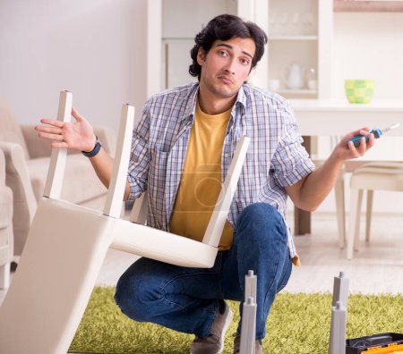Téléchargez les photos : Le jeune homme beau réparer chaise à la maison - en image libre de droit