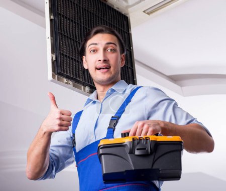 Téléchargez les photos : Le jeune réparateur réparer unité de climatisation de plafond - en image libre de droit