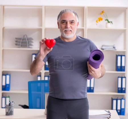 Foto de The white bearded old man employee doing exercises in the office - Imagen libre de derechos