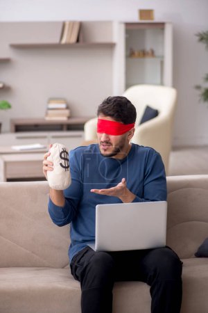 Photo for Blindfolded man holding moneybag at home - Royalty Free Image