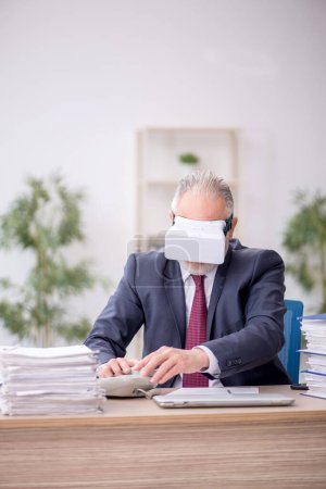 Photo for Old employee wearing virtual glasses at workplace - Royalty Free Image