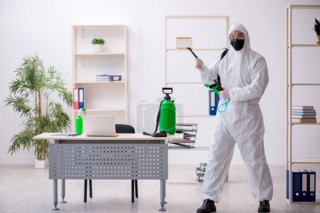 Téléchargez les photos : Jeune entrepreneur désinfectant le bureau pendant la pandémie - en image libre de droit