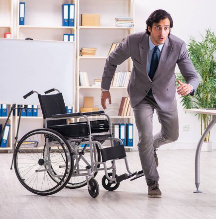 Téléchargez les photos : The young handsome employee in wheelchair at the office - en image libre de droit