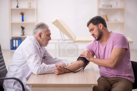 Foto de Médico viejo midiendo pacientes jóvenes presión arterial - Imagen libre de derechos