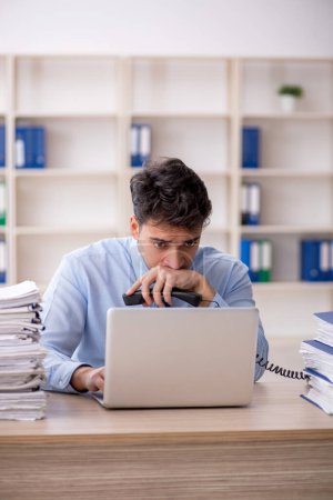 Téléchargez les photos : Young employee and too much work at workplace - en image libre de droit