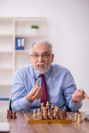 Foto de Viejo empleado jugando ajedrez en la oficina - Imagen libre de derechos