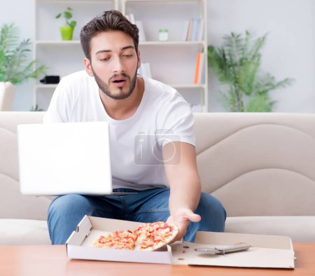 Téléchargez les photos : L'homme mangeant de la pizza ayant un plat à emporter à la maison détente au repos - en image libre de droit