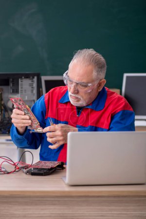 Foto de Hombre viejo reparador reparando computadoras en el aula - Imagen libre de derechos