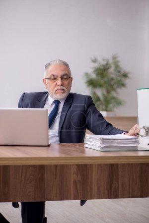 Téléchargez les photos : Old employee sitting at workplace - en image libre de droit