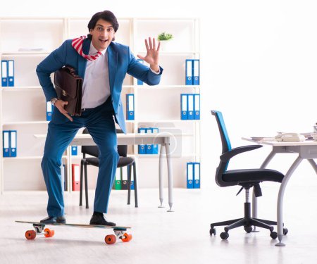 Téléchargez les photos : Le jeune homme d'affaires beau avec longboard dans le bureau - en image libre de droit