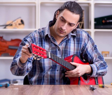 Téléchargez les photos : Le jeune réparateur beau réparateur de guitare - en image libre de droit