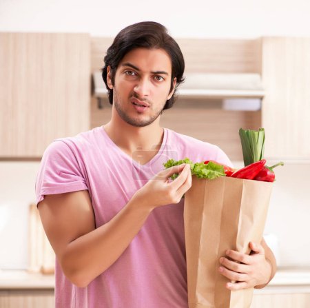 Téléchargez les photos : Le jeune homme beau avec des légumes dans la cuisine - en image libre de droit